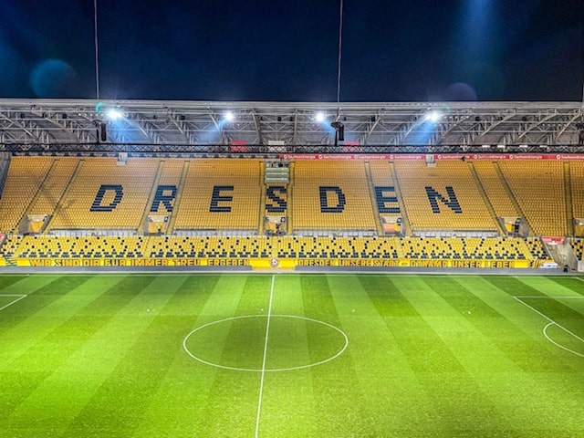 Beleuchtetes Stadion von Dynamo Dresden bei Nacht mit gelben Sitzreihen und dem Schriftzug 'DRESDEN' auf der Tribüne